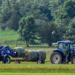 two tractors loading hay bales on a wagon